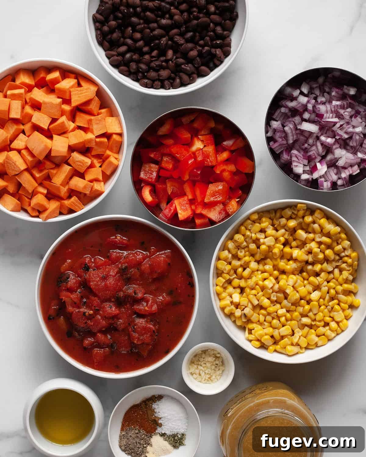 Hearty Sweet Potato Black Bean Chili 3 A flat lay photograph showcasing all the fresh and pantry ingredients for sweet potato chili, including peeled and diced sweet potatoes, canned black beans, corn, red bell peppers, chopped red onions, minced garlic, vegetable broth, and a selection of dried spices like chili powder and cumin.