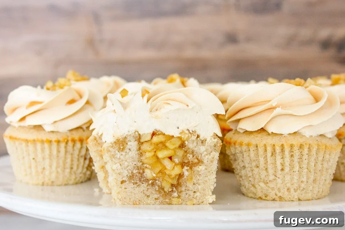 Caramel Apple Orchard Delights 2 A stunning cake stand brimming with perfectly frosted caramel apple cupcakes. One cupcake is artfully sliced in half, revealing the rich, spiced apple filling within its tender cinnamon cake base.