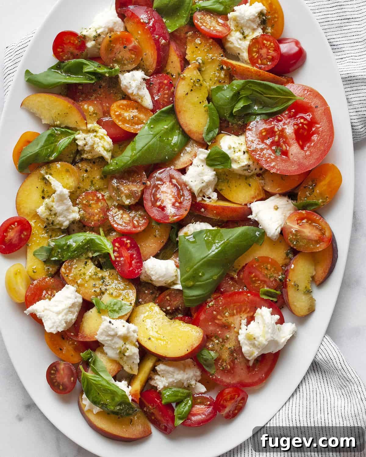 Summer Peach Caprese Salad 2 Detail image of peach caprese salad. A close-up shot of juicy peaches, colorful tomatoes, fresh mozzarella, and basil leaves drizzled with pesto vinaigrette, artfully arranged on a white platter.