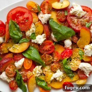 Summer Peach Caprese Salad 7 Detail image of peach caprese salad. A close-up shot of juicy peaches, colorful tomatoes, fresh mozzarella, and basil leaves drizzled with pesto vinaigrette, artfully arranged on a white platter.