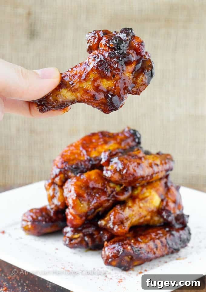 Sticky Sweet Chili Baked Wings 2 A stack of perfectly baked chicken wings with one wing being held up, showcasing its crispy skin and rich sauce.