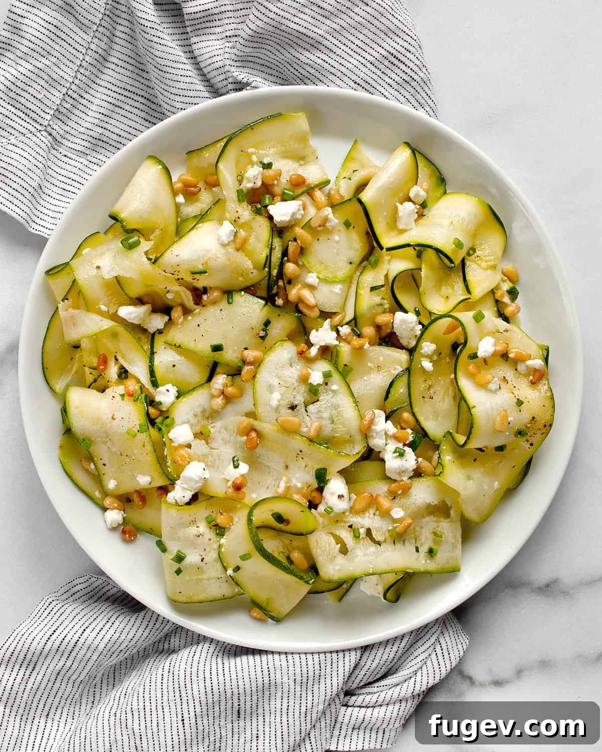 Zesty Zucchini Salad with Feta and Pine Nuts 2 Vibrant zucchini ribbon salad garnished with feta and toasted pine nuts on a white plate.