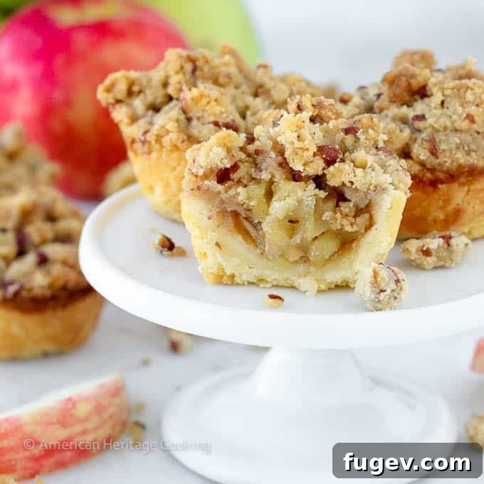 Petite Apple Pastries 2 Delicious mini apple pie with a golden pecan crumble topping, sliced in half to show the spiced apple filling and flaky cream cheese crust.