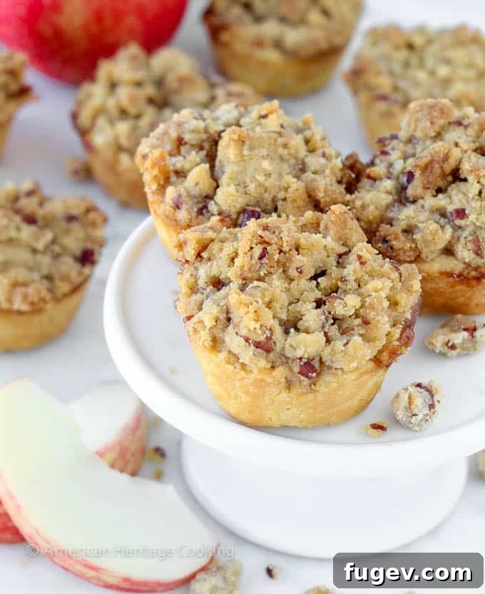 Petite Apple Pastries 3 A charming display of mini apple pies topped with pecan crumble, arranged beautifully on a small white cake stand.