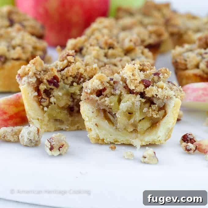 Petite Apple Pastries 4 Close-up of a mini apple pie, revealing the tender cream cheese crust and spiced apple filling, artfully placed on a white surface.