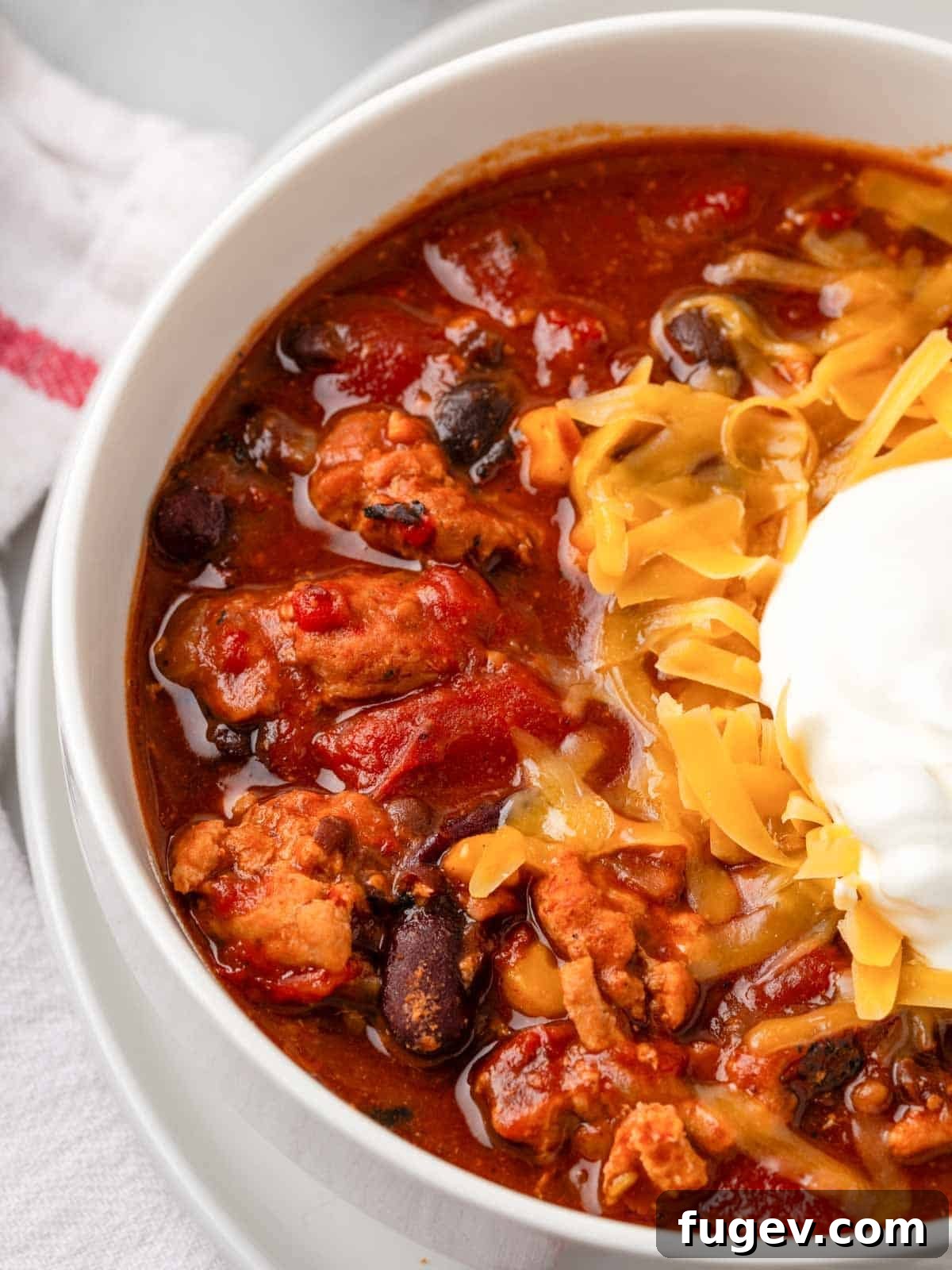 Smoldering Chipotle Chili 2 A large white bowl filled with rich chipotle chili, garnished with a dollop of sour cream and shredded cheese, invitingly presented.
