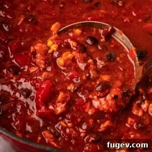 A close-up of a ladle scooping a rich, hearty chipotle chili from a pot, showcasing its inviting texture and warmth.