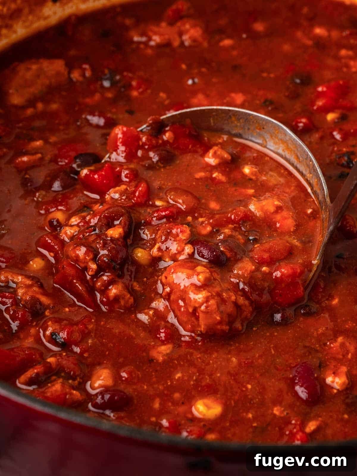 Smoldering Chipotle Chili 4 A ladle scooping rich, steaming chili from a Dutch oven, showing the hearty texture with beans and corn visible, ready to be served.