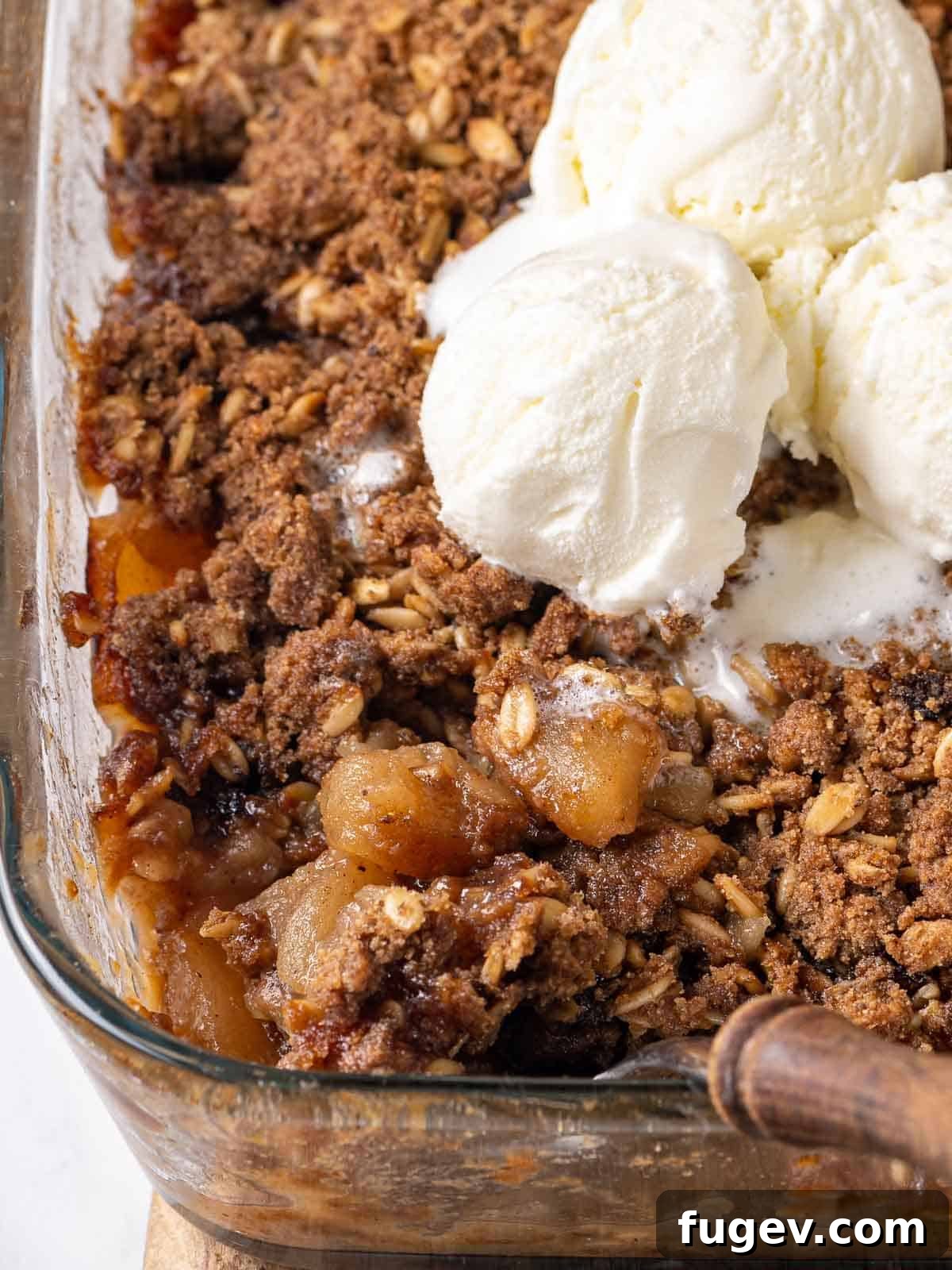 Effortless Apple Crisp Perfection 2 A golden brown apple crisp in a baking dish, generously topped with a scoop of melting vanilla ice cream, ready to be served.
