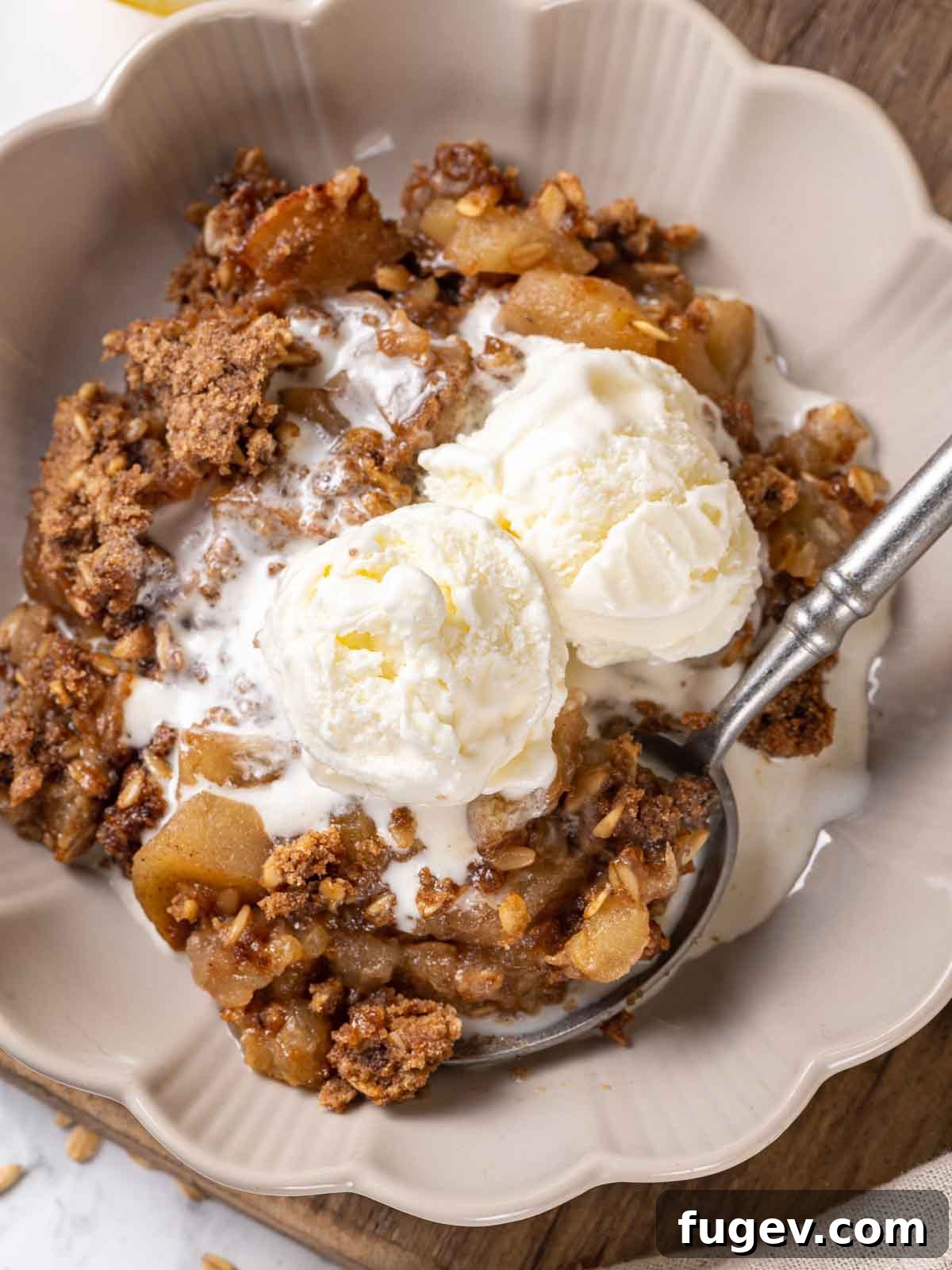 Effortless Apple Crisp Perfection 3 A bowl of warm apple crisp topped with vanilla ice cream and a pewter spoon, showcasing the delicious crispy brown sugar oat topping.