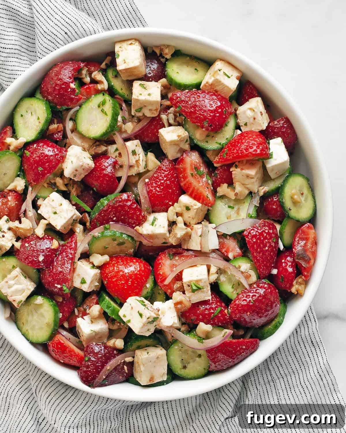Strawberry Feta Sparkle 2 A vibrant and refreshing strawberry cucumber feta salad served in a large white bowl, garnished with fresh herbs, showcasing the red strawberries, green cucumbers, and white feta cheese cubes.
