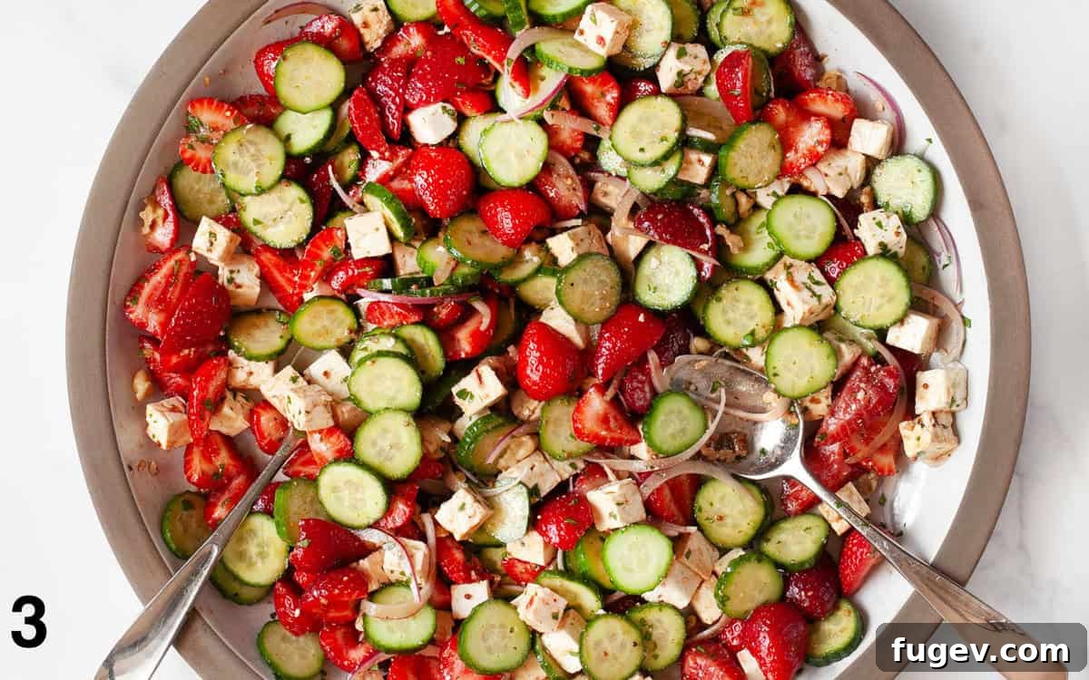 Strawberry Feta Sparkle 5 The strawberry feta salad ingredients are thoroughly tossed with the honey balsamic vinaigrette in a large white bowl, ensuring an even coating on all components.