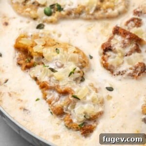 Close-up of a perfectly cooked pork chop with mushroom and thyme sauce in a skillet.
