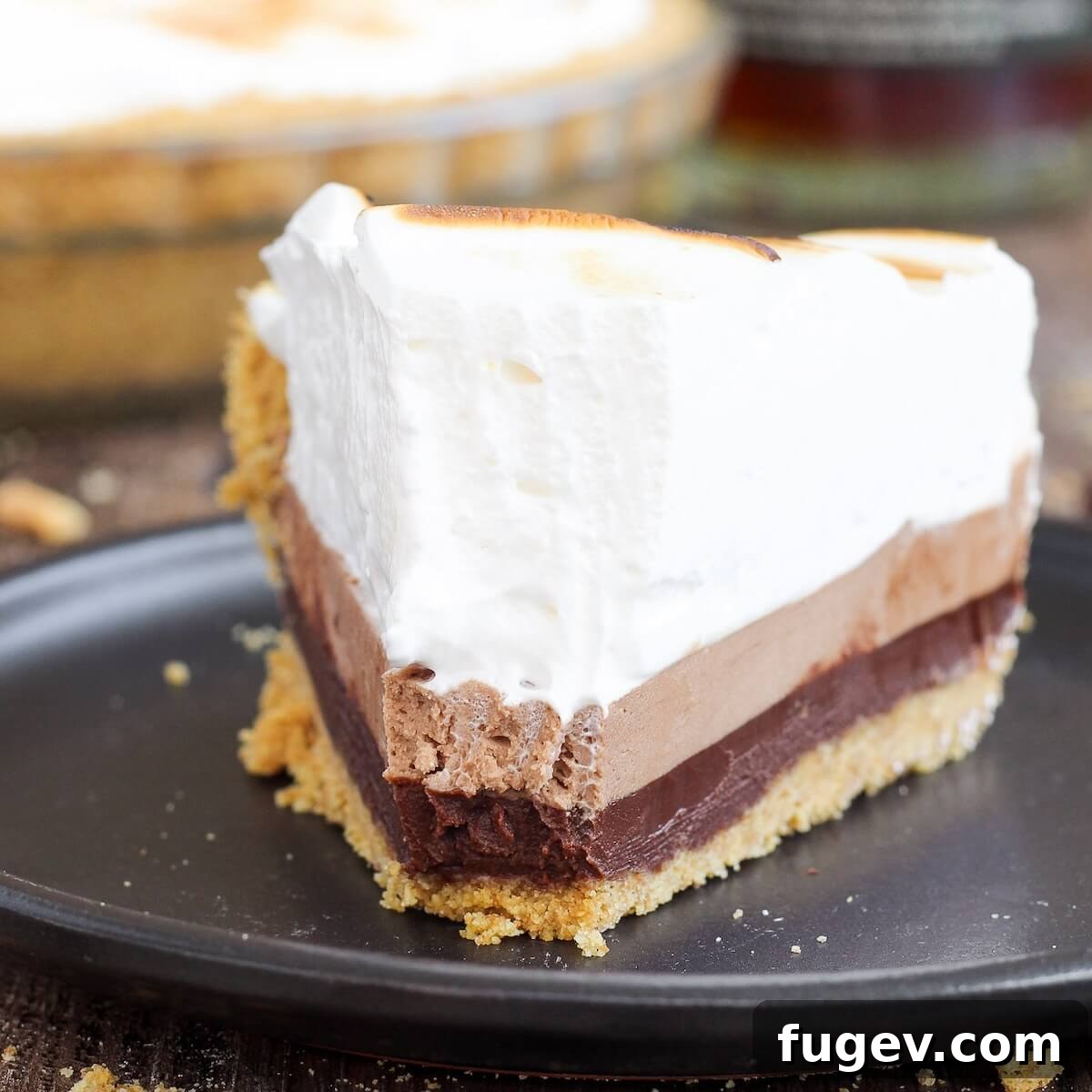 Pillowy Marshmallow Perfection 10 A slice of whiskey s'mores pie topped with beautifully toasted marshmallow frosting on a sleek black plate.