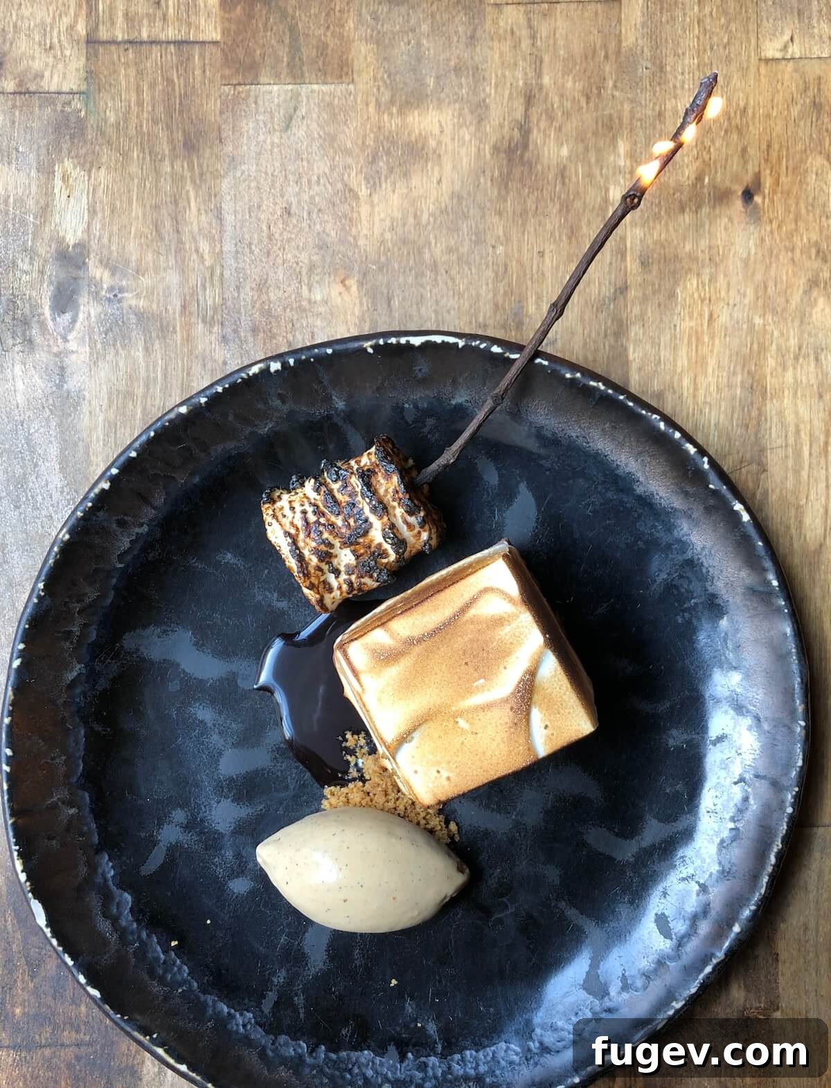 Pillowy Marshmallow Perfection 3 A plated s'mores dessert on a sleek black plate, elegantly topped with toasted marshmallow frosting.