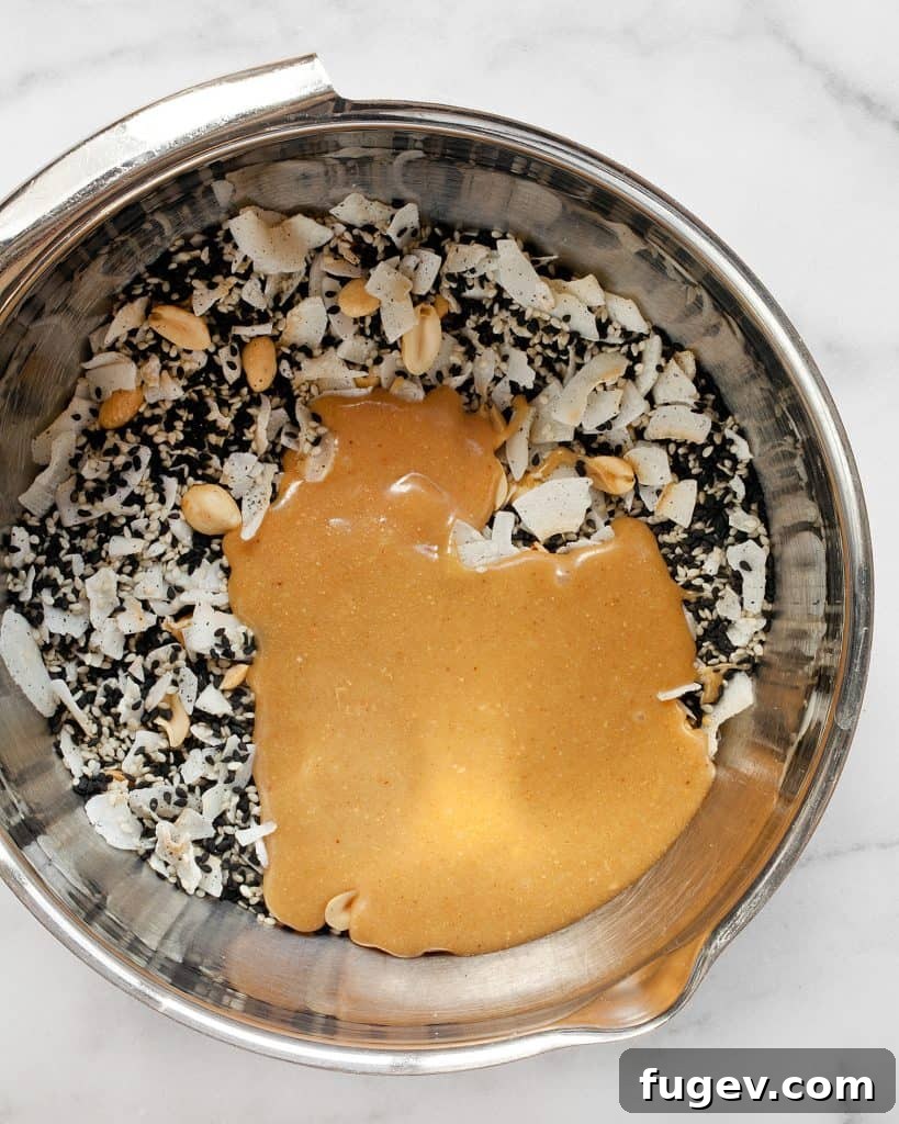 Golden Sesame Peanut Bars 7 Mixing bowl with sesame seeds, peanuts, coconut flakes, and peanut butter mixture being stirred