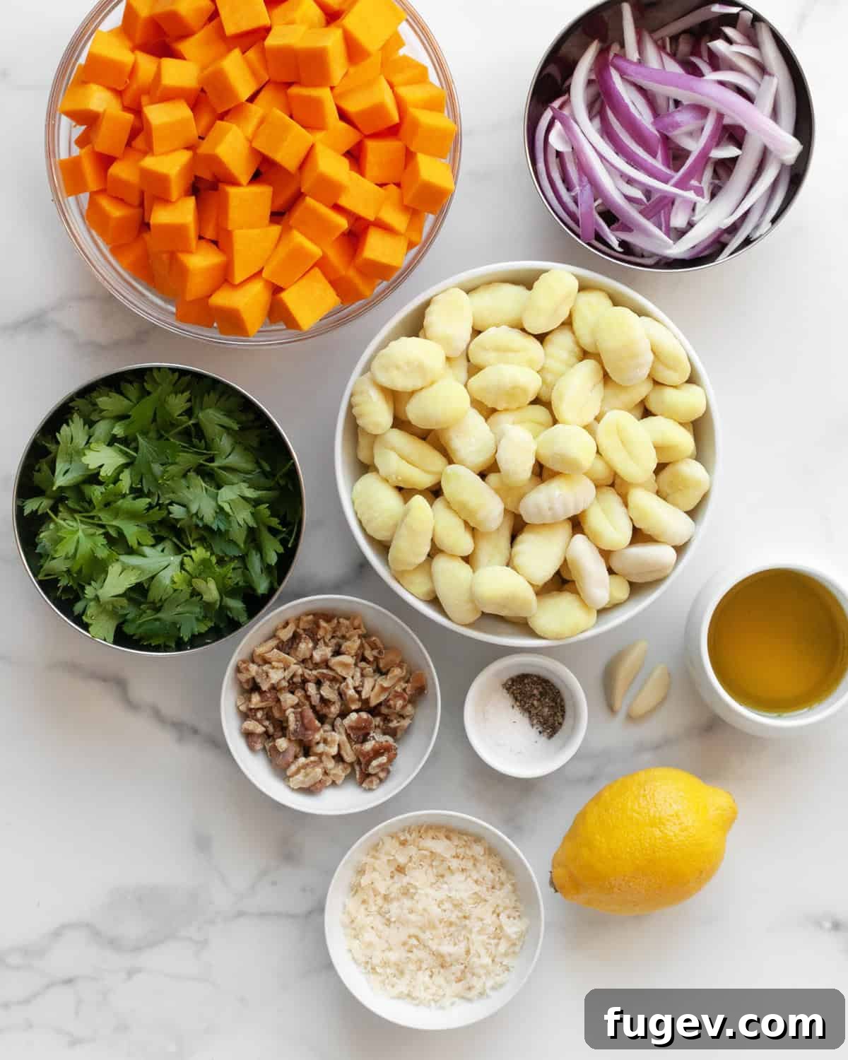 One Pan Butternut Gnocchi with Bright Parsley Pesto 3 A vibrant selection of ingredients for sheet pan butternut squash gnocchi, including cubed butternut squash, sliced red onions, gnocchi, fresh parsley, garlic cloves, Parmesan cheese, walnuts, lemon, olive oil, and seasonings.