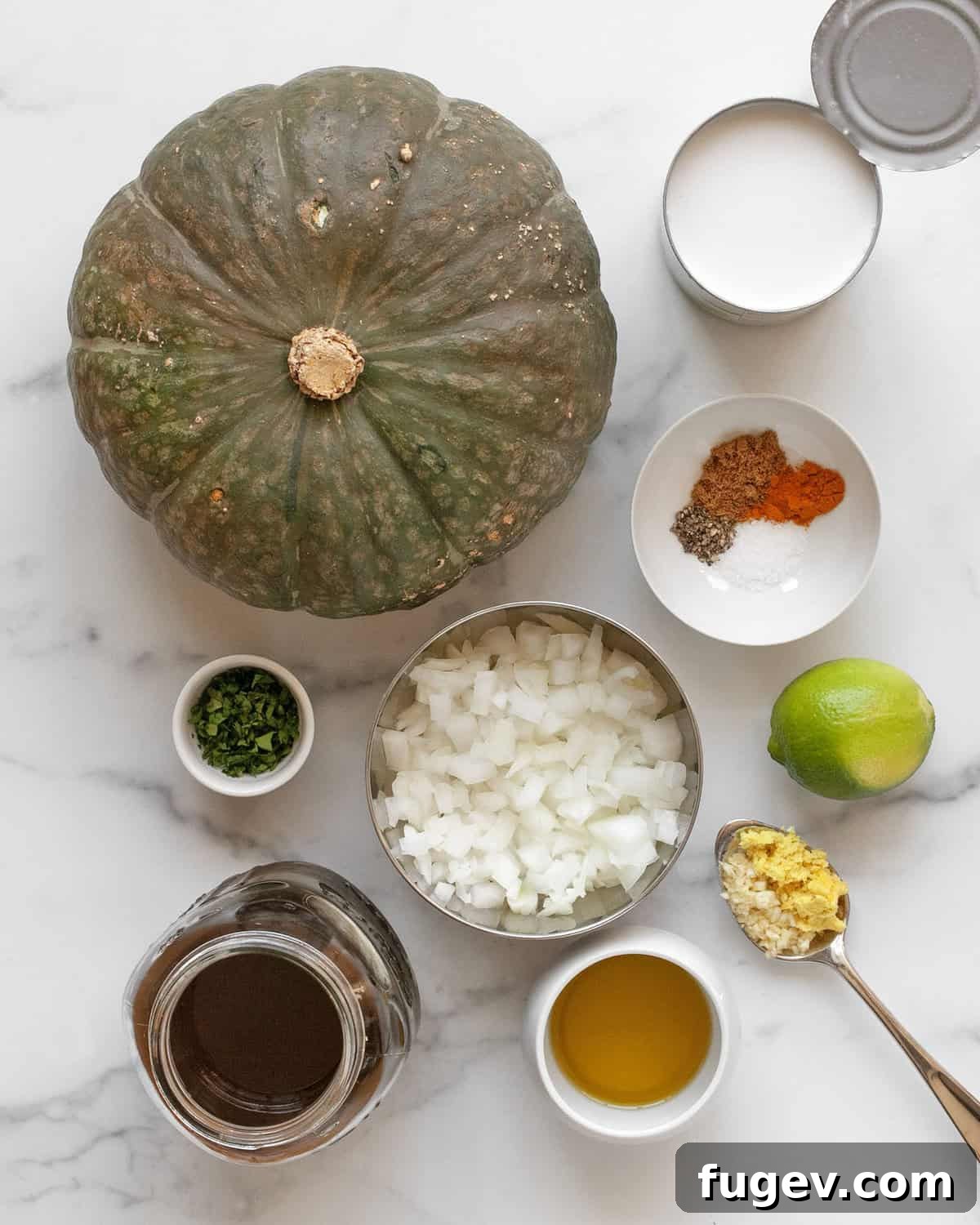 Velvet Roasted Kabocha Soup 3 A vibrant collection of fresh ingredients: kabocha squash, a can of coconut milk, an onion, fresh ginger, garlic cloves, lime, olive oil, and various spices.