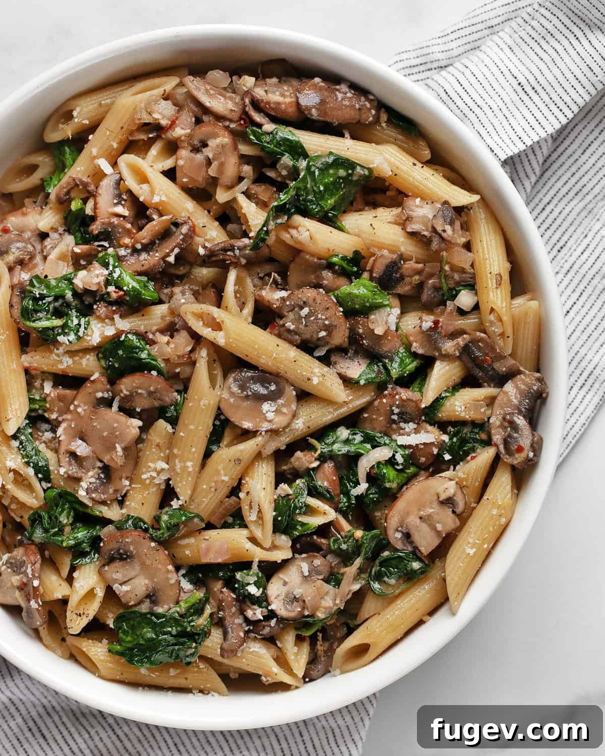 A vibrant bowl of mushroom spinach pasta, garnished with fresh herbs and grated Parmesan.