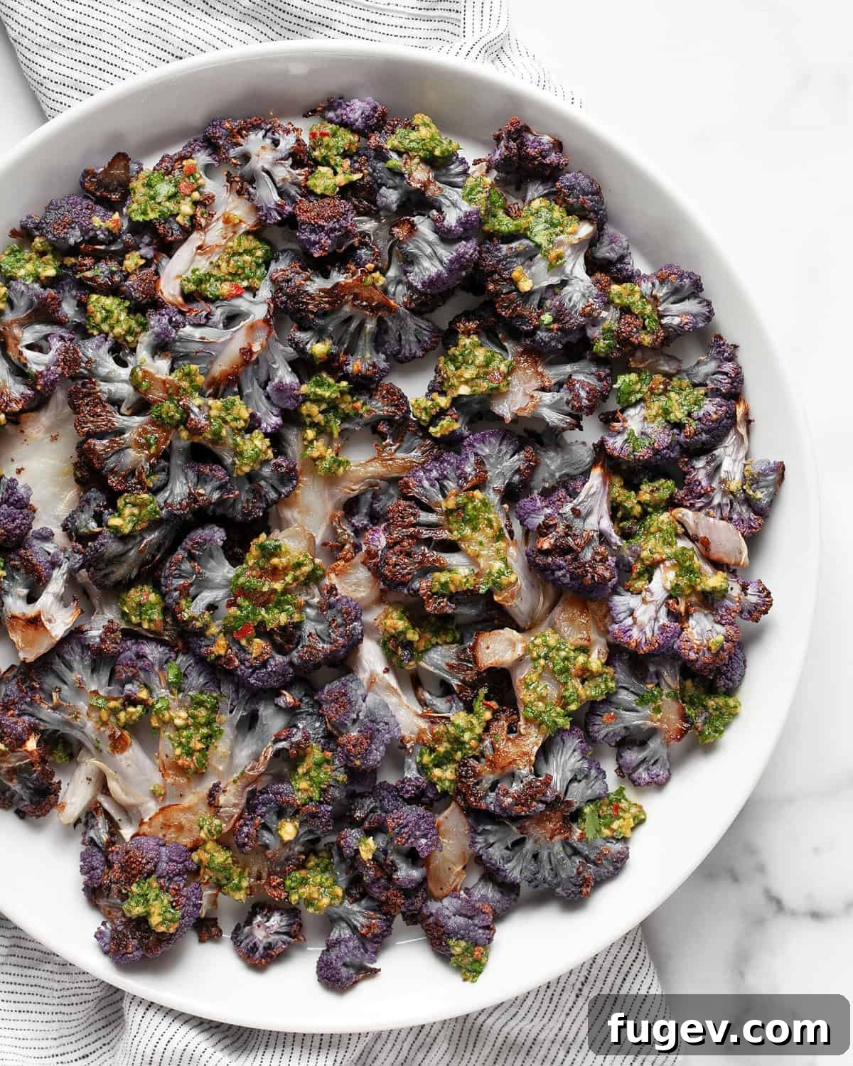 Roasted Amethyst Florets with Zesty Cilantro Burst 7 A close-up shot of roasted purple cauliflower florets on a plate, garnished with fresh cilantro pesto and a sprinkle of chopped peanuts.