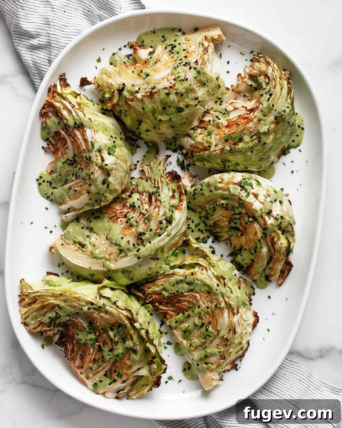 Perfectly Roasted Cabbage Steaks 2 Golden brown roasted cabbage wedges artfully arranged on an oval platter, drizzled with a vibrant green tahini sauce.