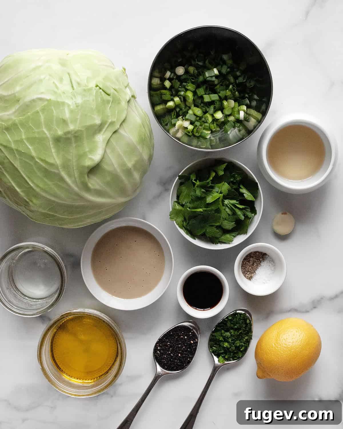 Perfectly Roasted Cabbage Steaks 3 A flat lay photograph showcasing all the fresh ingredients needed for roasted cabbage: green cabbage, scallions, parsley, tahini, lemon, olive oil, rice vinegar, garlic, salt, pepper, and water.