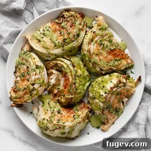 Roasted cabbage wedges on a plate, drizzled with tahini sauce and garnished with sesame seeds.