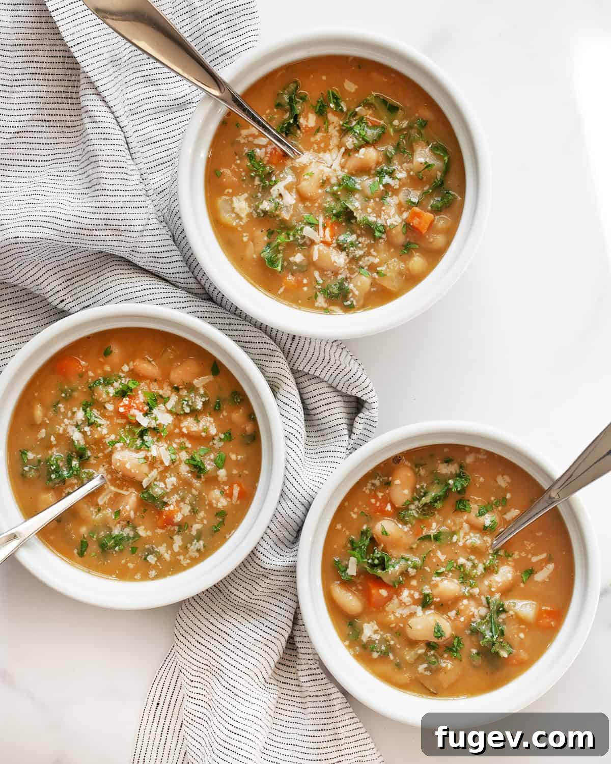 Velvety Tuscan White Bean Soup 7 Three bowls of creamy Italian white bean soup, artfully arranged on a wooden surface.