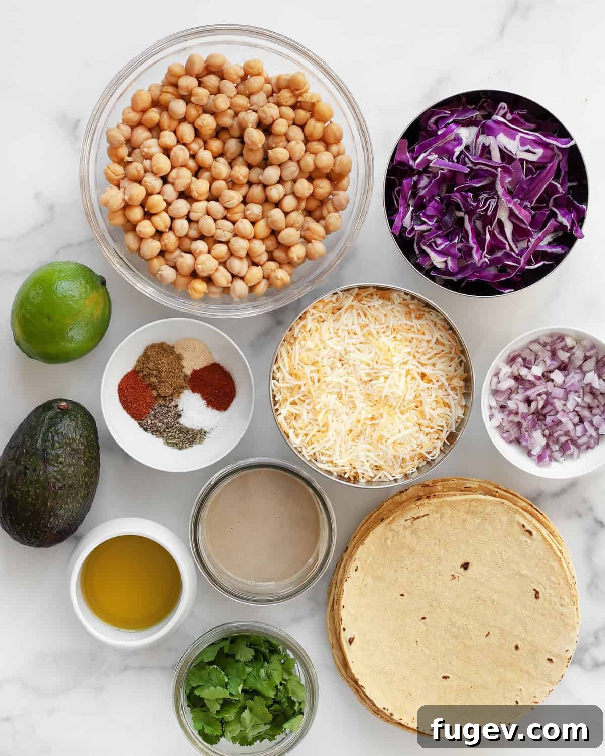 Oven-Crisped Chickpea Tacos 3 A flat lay of fresh ingredients including chickpeas, corn tortillas, shredded cabbage, cheese, red onions, taco seasonings, lime, avocado, and olive oil.
