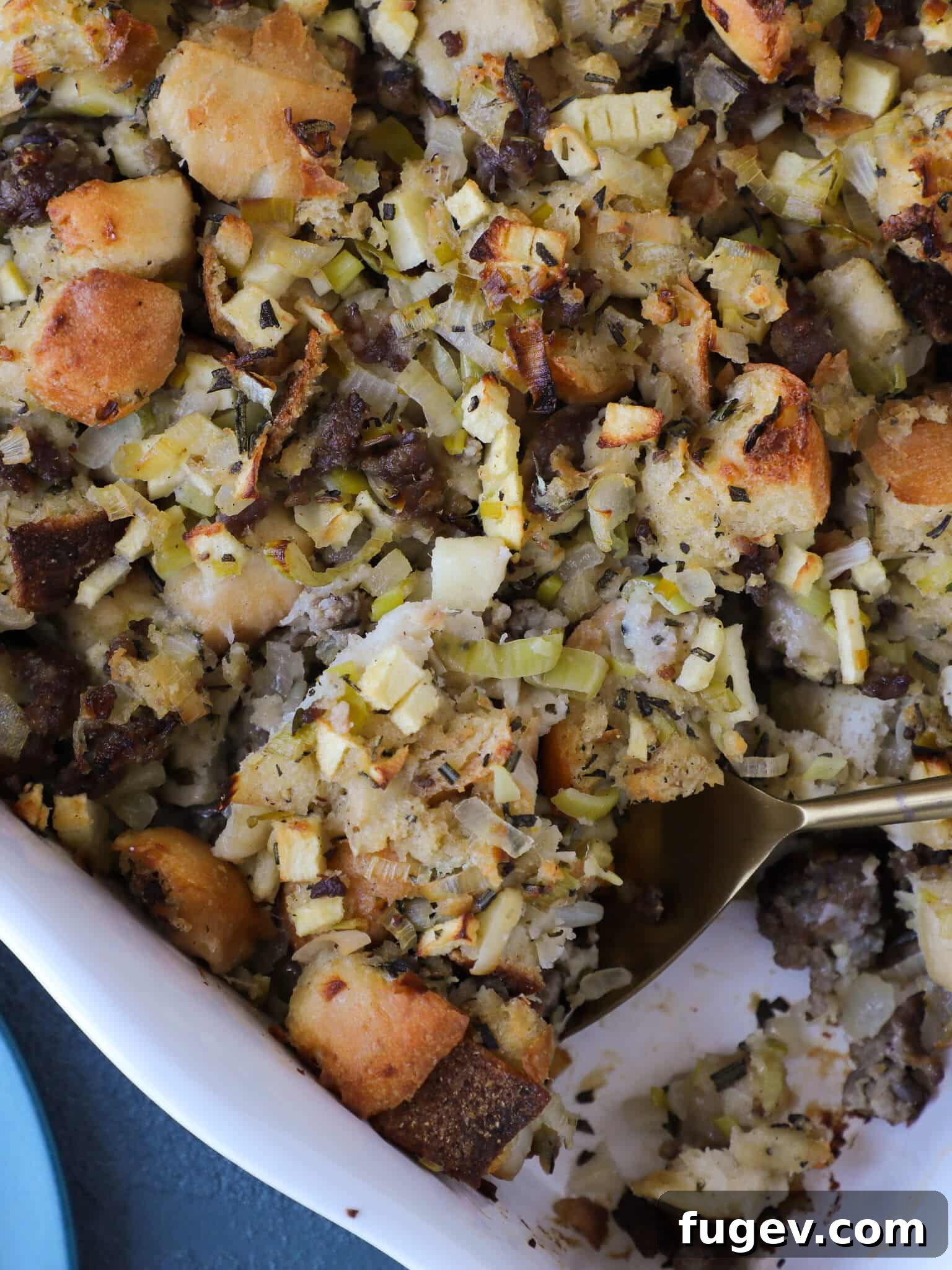Golden Apple Sausage Stuffing 2 Apple Sage Sausage Stuffing in a white baking dish with a spoon, highlighting its golden crust.