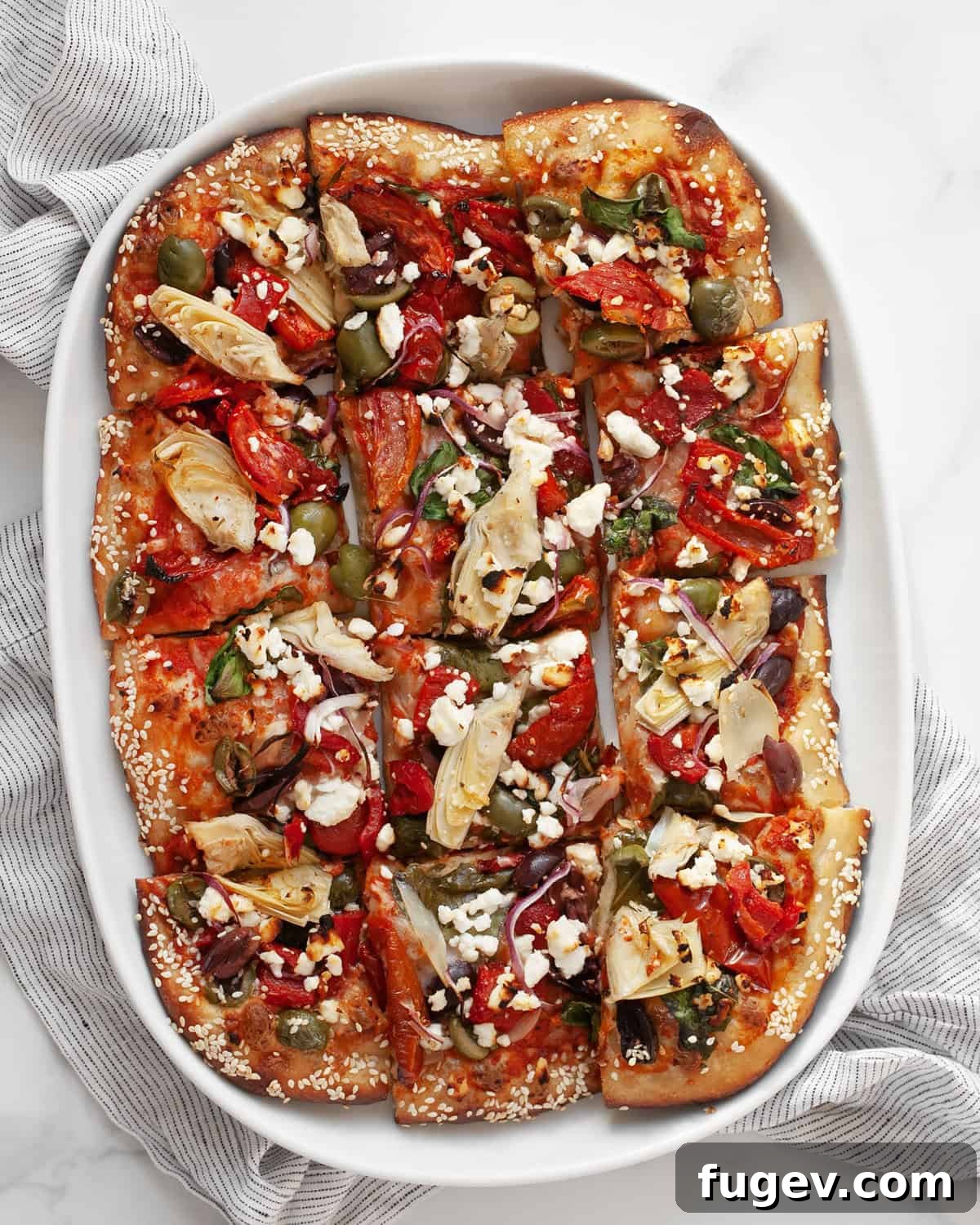 Mediterranean Harvest Pizza 2 Mediterranean pizza cut into squares on a serving plate, showcasing colorful toppings.