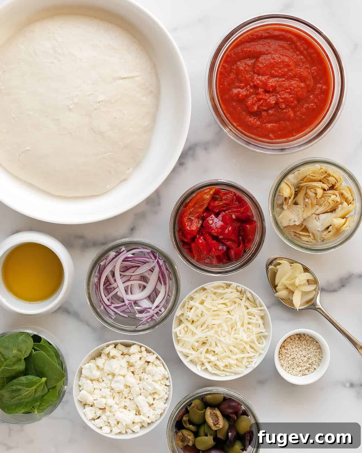 Mediterranean Harvest Pizza 3 A vibrant flat lay of all the Mediterranean pizza ingredients: dough, mozzarella, feta, tomato sauce, olives, sun-dried tomatoes, artichokes, red peppers, onions, garlic, and olive oil.