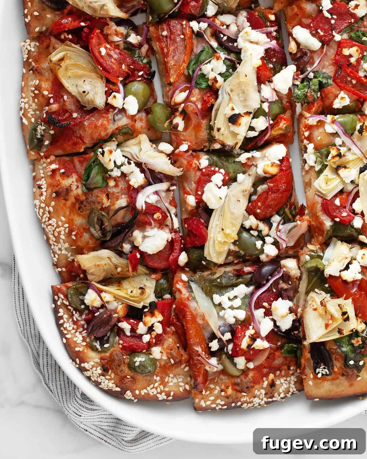 Mediterranean Harvest Pizza 7 Mediterranean pizza, freshly baked and cut into perfect squares on a white serving plate.