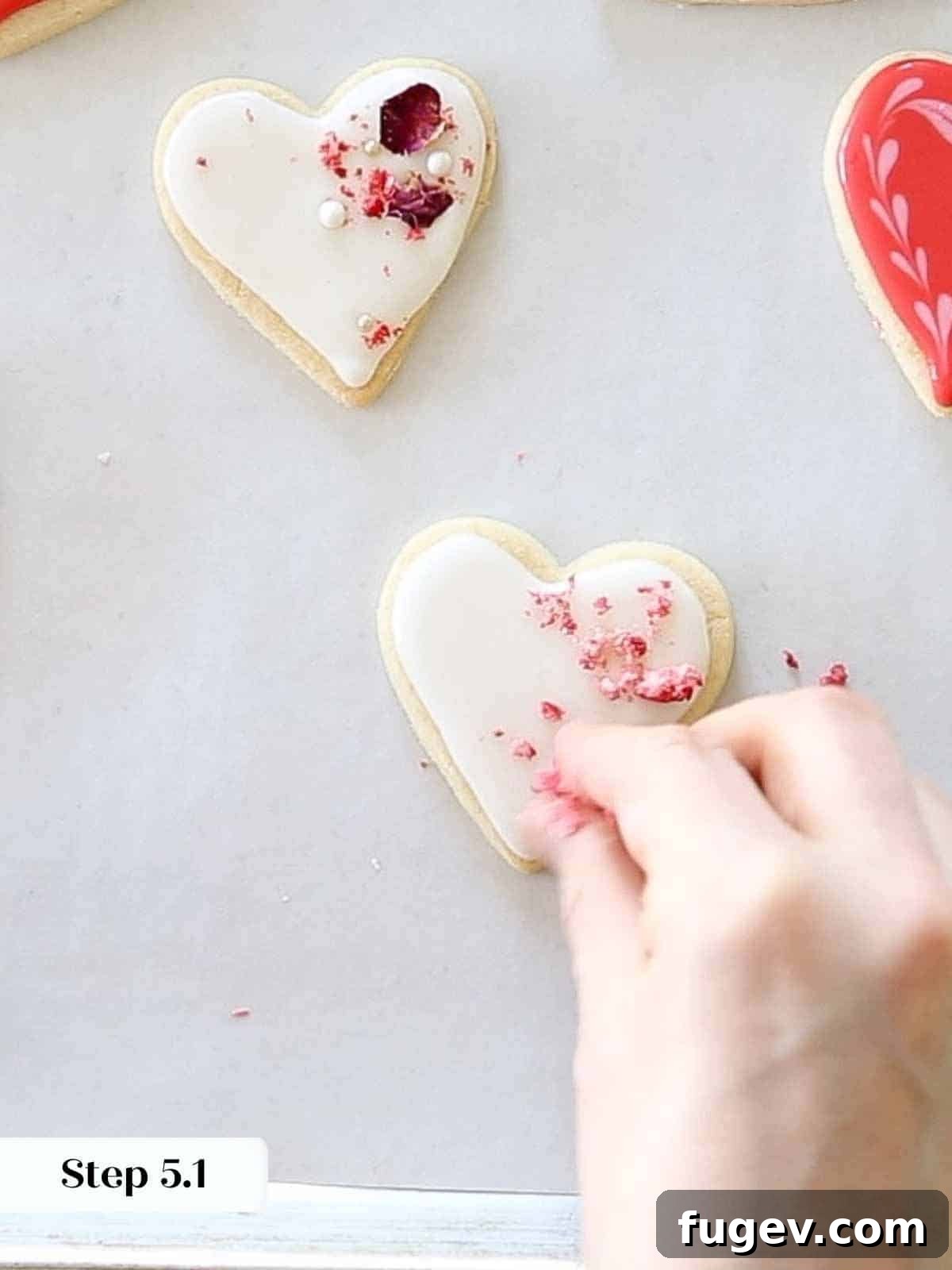 Cupid's Confections 18 Sprinkling delicate dehydrated strawberries over white royal icing hearts.