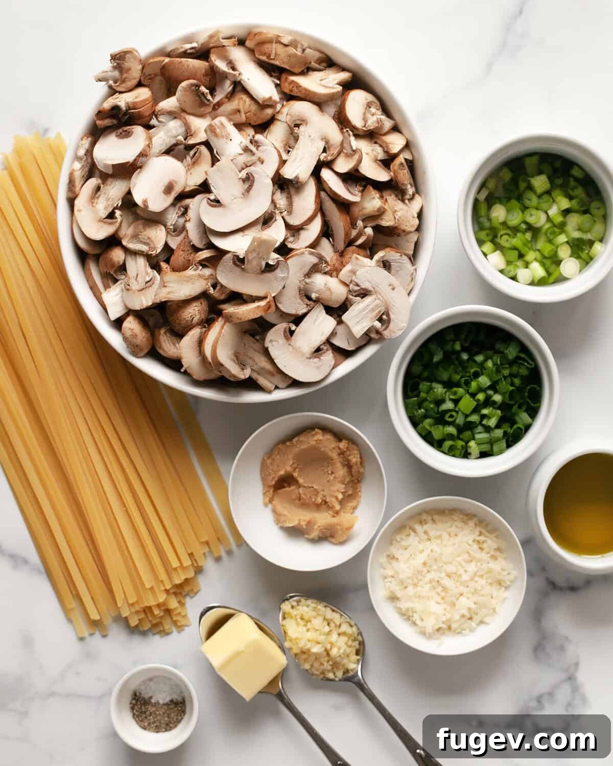 Umami-Packed Miso Mushroom Pasta 3 A flat lay photograph showcasing all the fresh ingredients needed for miso mushroom pasta: sliced mushrooms, white miso paste, fettuccine, chopped scallions, grated parmesan cheese, minced garlic, a bottle of olive oil, and small bowls of salt and pepper.