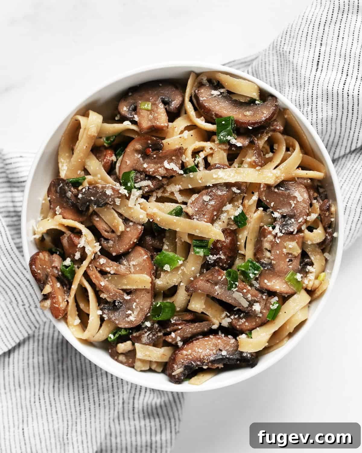 Umami-Packed Miso Mushroom Pasta 7 A close-up shot of a bowl filled with steaming miso mushroom pasta, garnished with fresh chopped green scallions and a light dusting of parmesan cheese.