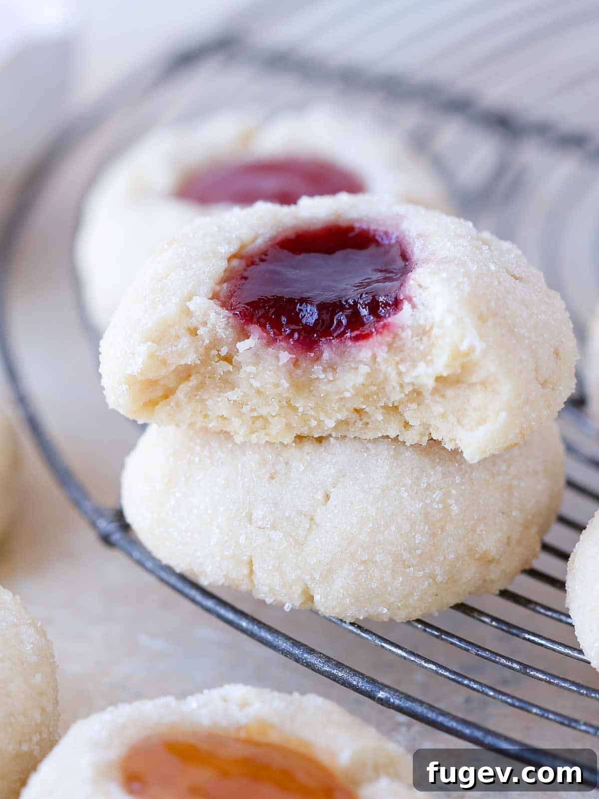 Perfectly Jammed Thumbprints 12 Another view of a broken thumbprint cookie on a wire rack, emphasizing its soft texture and the rich jam filling. The image reinforces the cookie's internal quality.