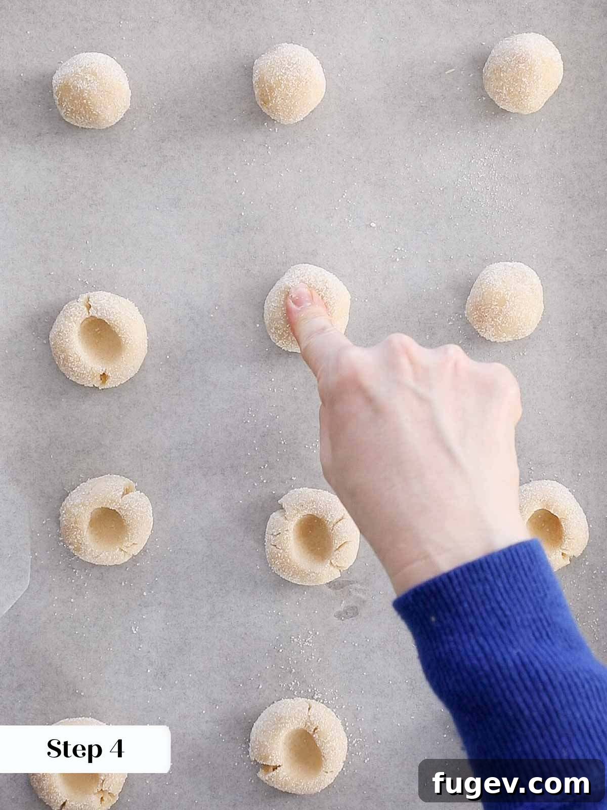 Perfectly Jammed Thumbprints 8 A finger gently pressing into a cookie dough ball on a baking sheet to create the signature thumbprint indentation. The image captures the careful technique.