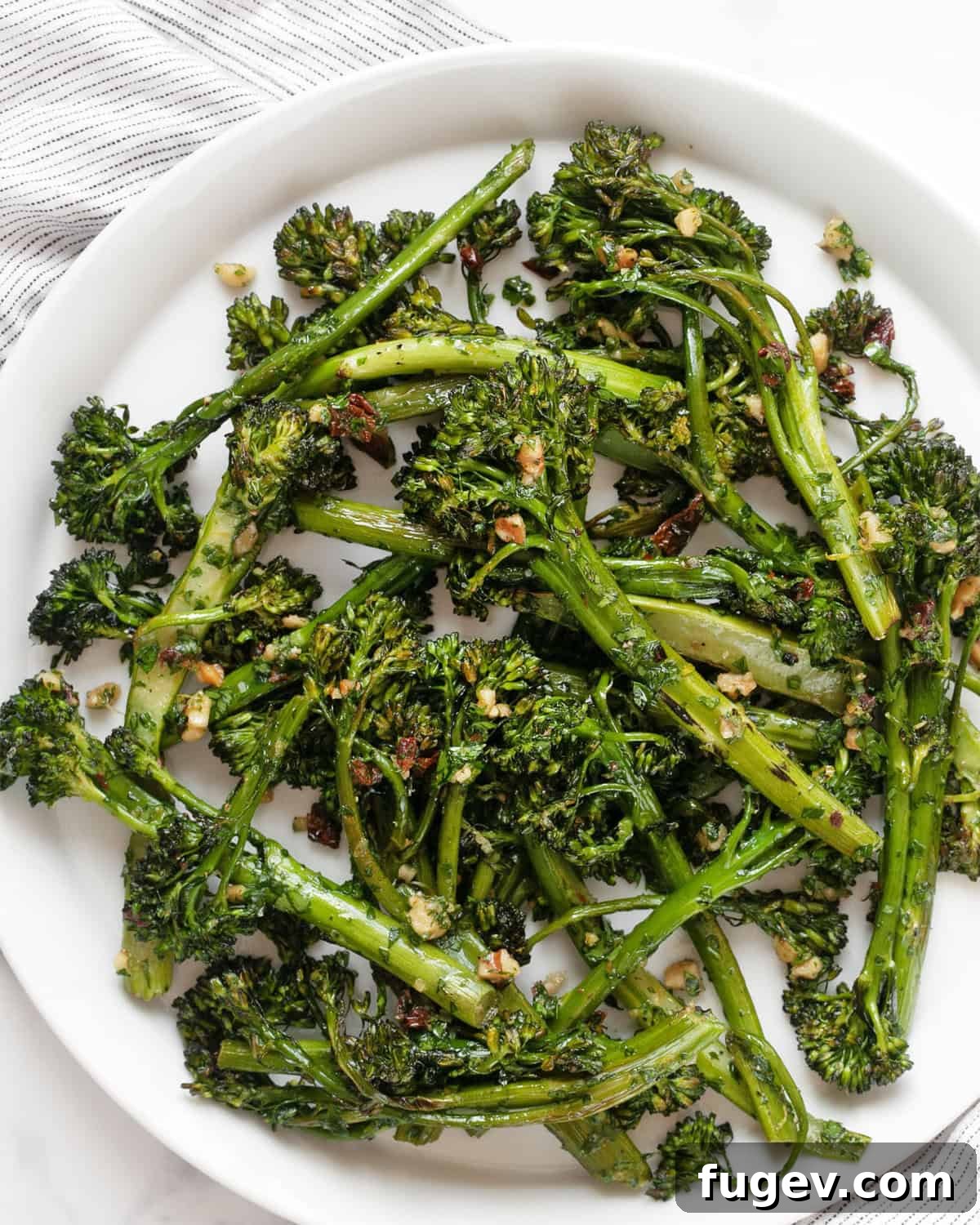 Crisp Roasted Broccolini with Sun Kissed Tomato Gremolata 2 Roasted broccolini garnished with sun-dried tomato gremolata on a white plate, ready to serve.