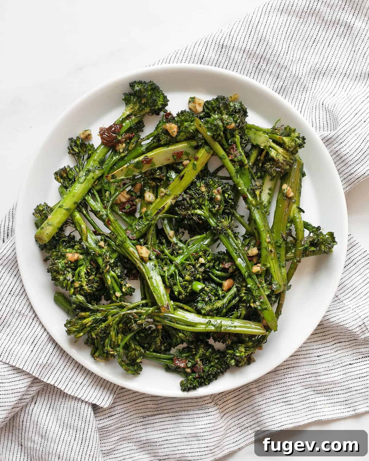 Crisp Roasted Broccolini with Sun Kissed Tomato Gremolata 6 A close-up shot of roasted broccolini with sun-dried tomato gremolata on a white plate, highlighting the texture and vibrant colors.