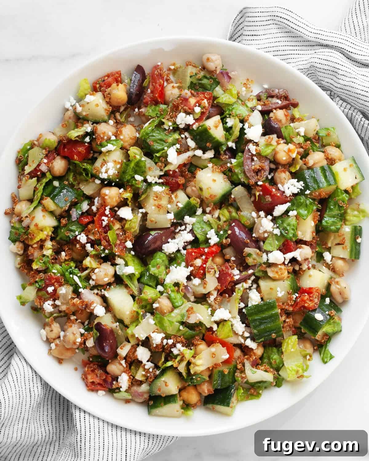 Golden Quinoa Mediterranean Delight 7 Individual serving of Mediterranean chopped salad with crispy quinoa on a white plate, ready to be enjoyed.