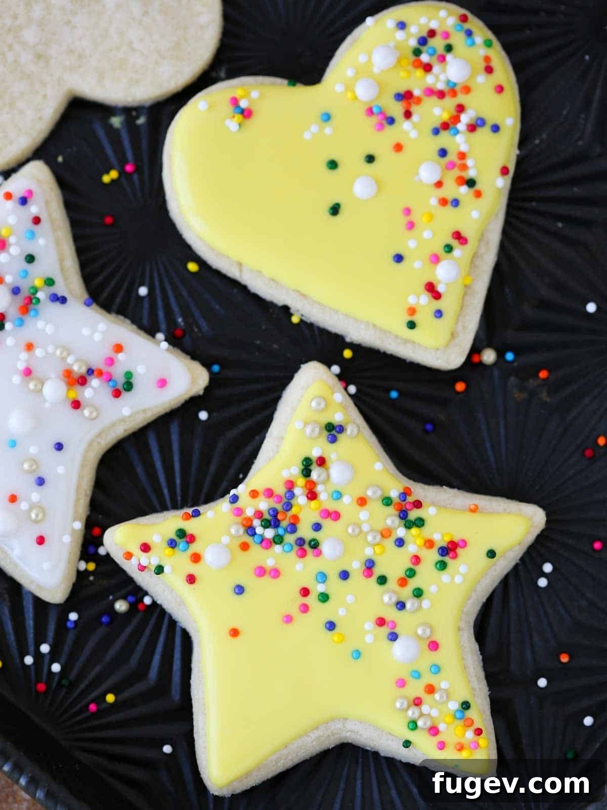 Foolproof Royal Icing with Meringue Powder 6 Bright yellow star and heart cookies arranged on a black tray, demonstrating the crisp lines and vibrant colors achieved with gel food coloring in royal icing.