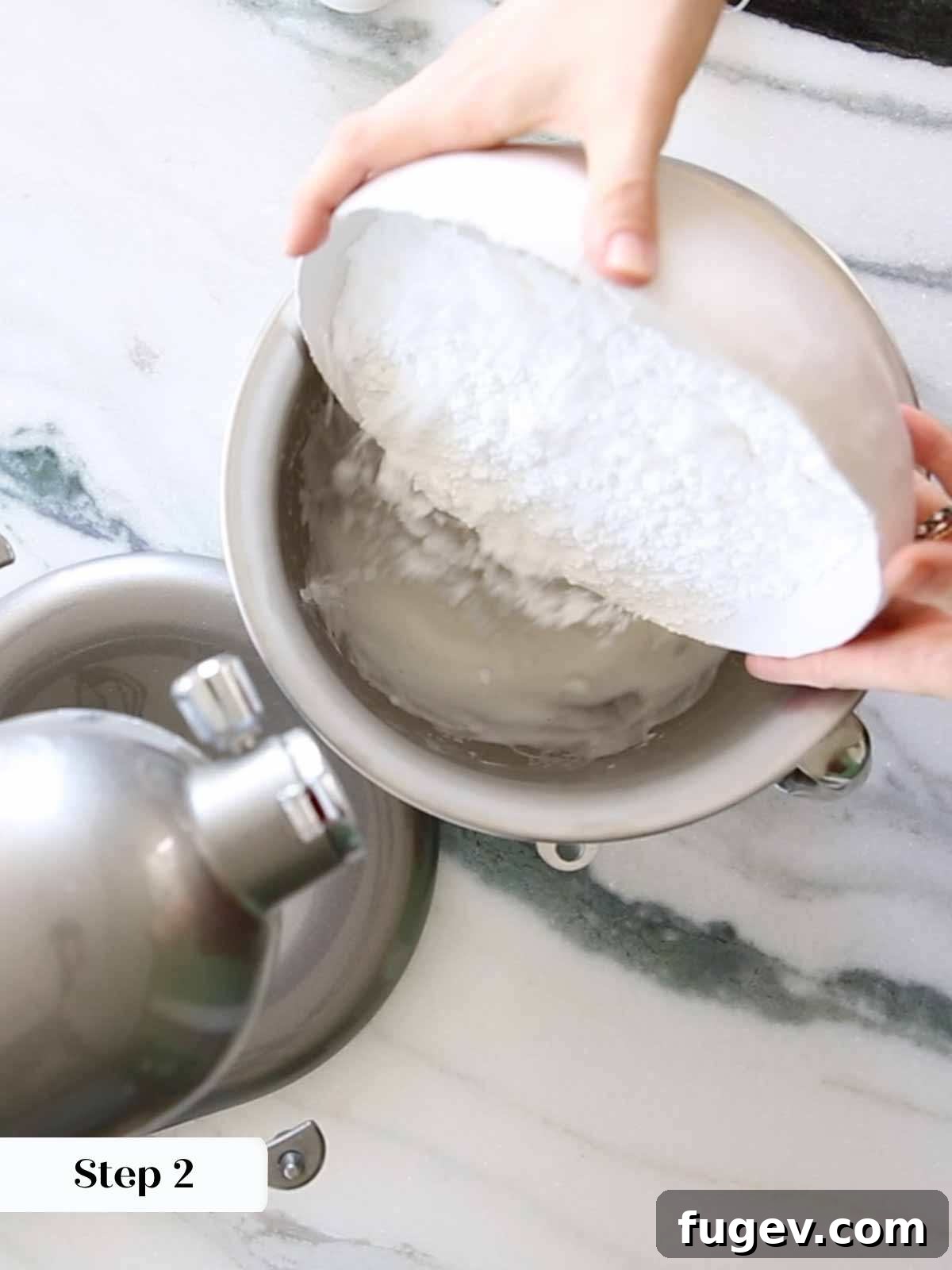 Foolproof Royal Icing with Meringue Powder 8 The process of adding powdered sugar to the whipped meringue mixture in a stand mixer, demonstrating the next step in creating royal icing.