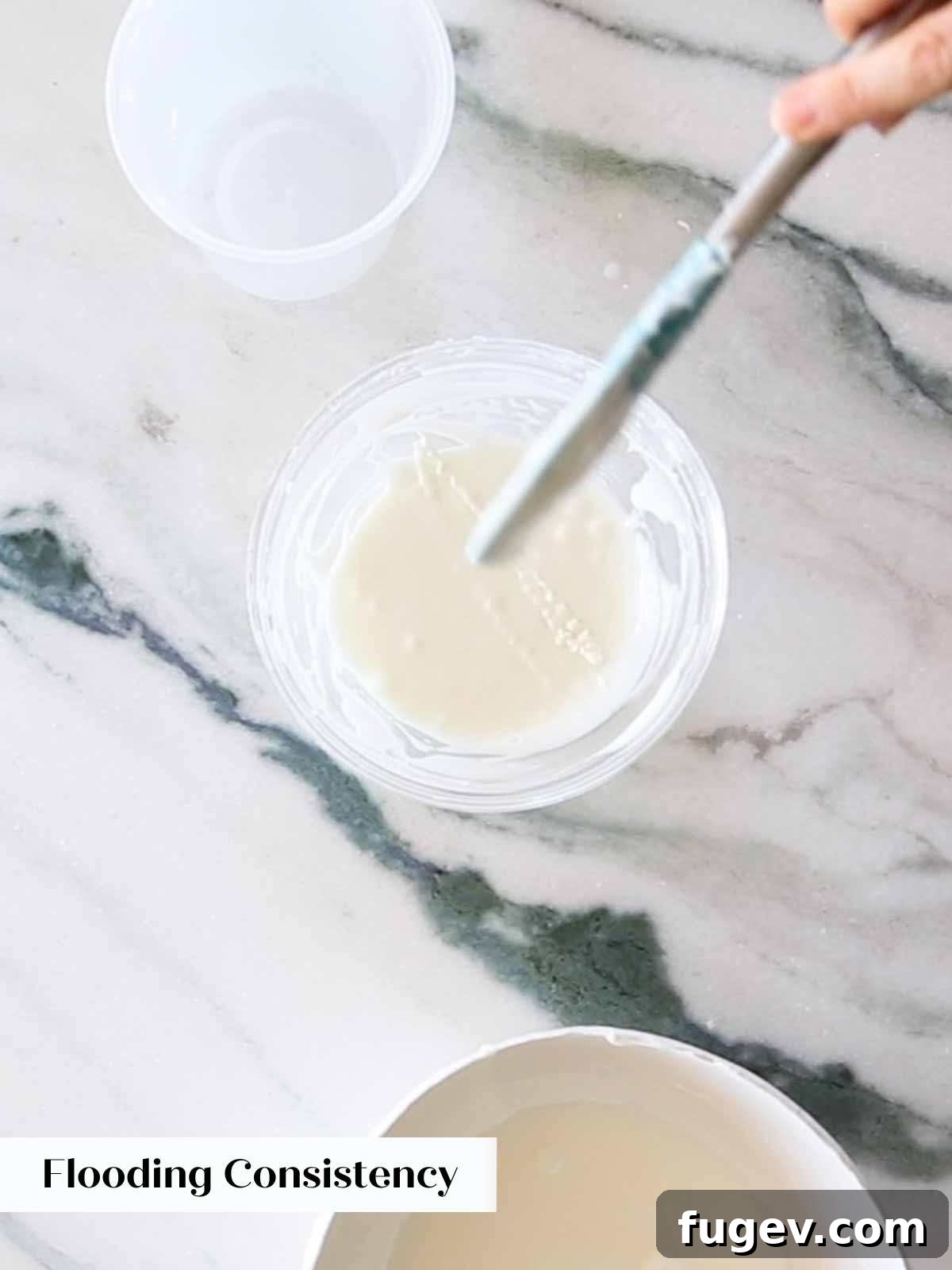Foolproof Royal Icing with Meringue Powder 10 A close-up image showing the perfect flooding consistency of royal icing, where the lifted icing quickly melts back into the main bowl.