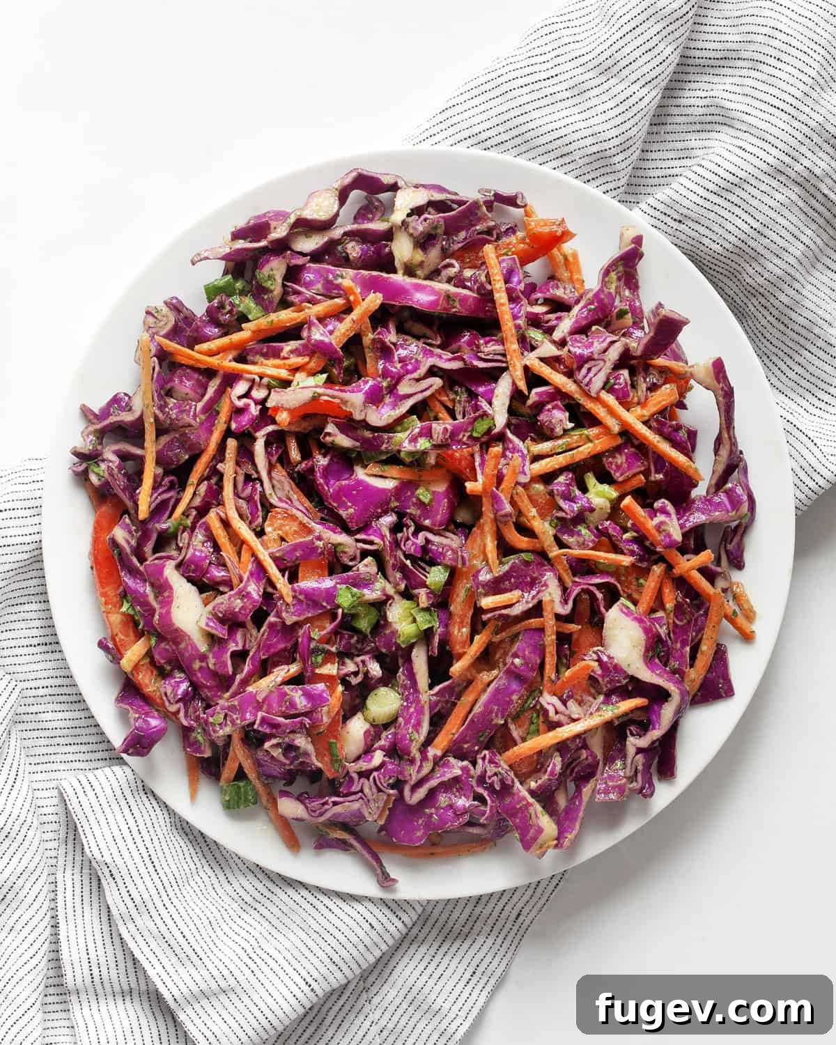 Vibrant Red Cabbage Slaw 6 A serving of vibrant red cabbage slaw artfully arranged on a white plate, garnished with fresh cilantro and a lime wedge, highlighting its appetizing presentation.