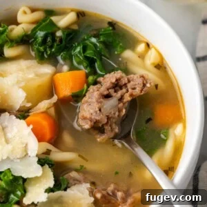 Close up view of Italian sausage soup in a white bowl with a spoon, showcasing its rich texture and ingredients.