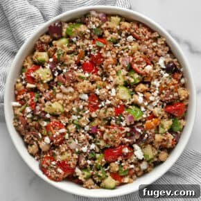 Quinoa salad in a large bowl, featuring chickpeas, roasted tomatoes, cucumbers, olives, and feta.