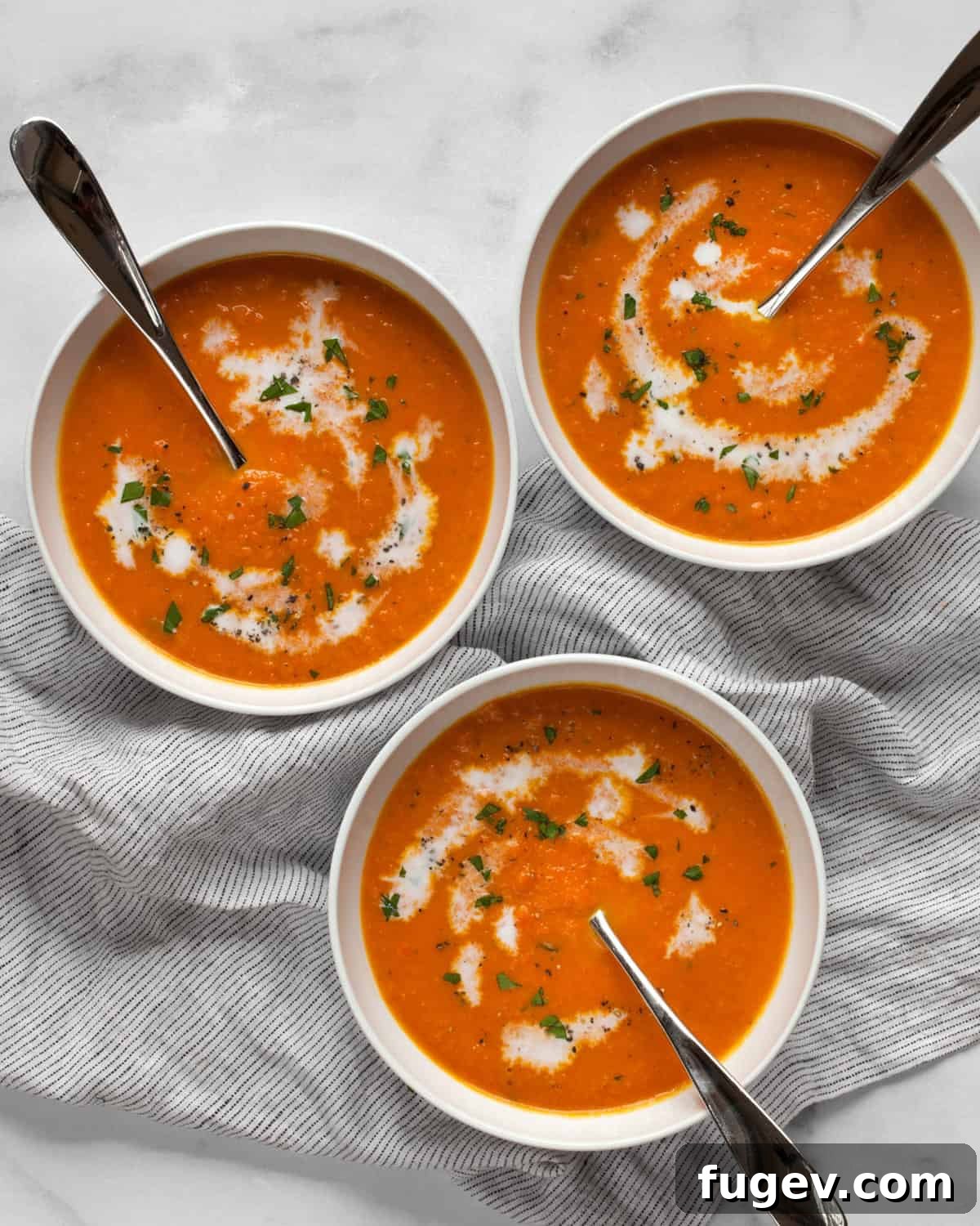 Golden Ginger Carrot Elixir 2 Three bowls of vibrant carrot ginger soup, beautifully garnished with a swirl of coconut milk and a sprinkle of fresh parsley.