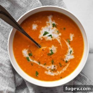 A vibrant bowl of vegan carrot ginger soup, garnished with a swirl of coconut milk and fresh herbs.