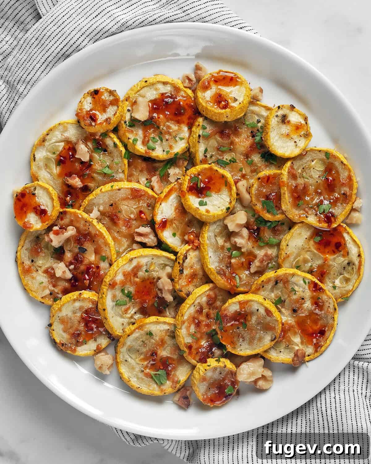 Sweet Heat Parmesan Roasted Squash 2 Parmesan roasted yellow squash drizzled with hot honey on a plate, garnished with fresh herbs and toasted walnuts.